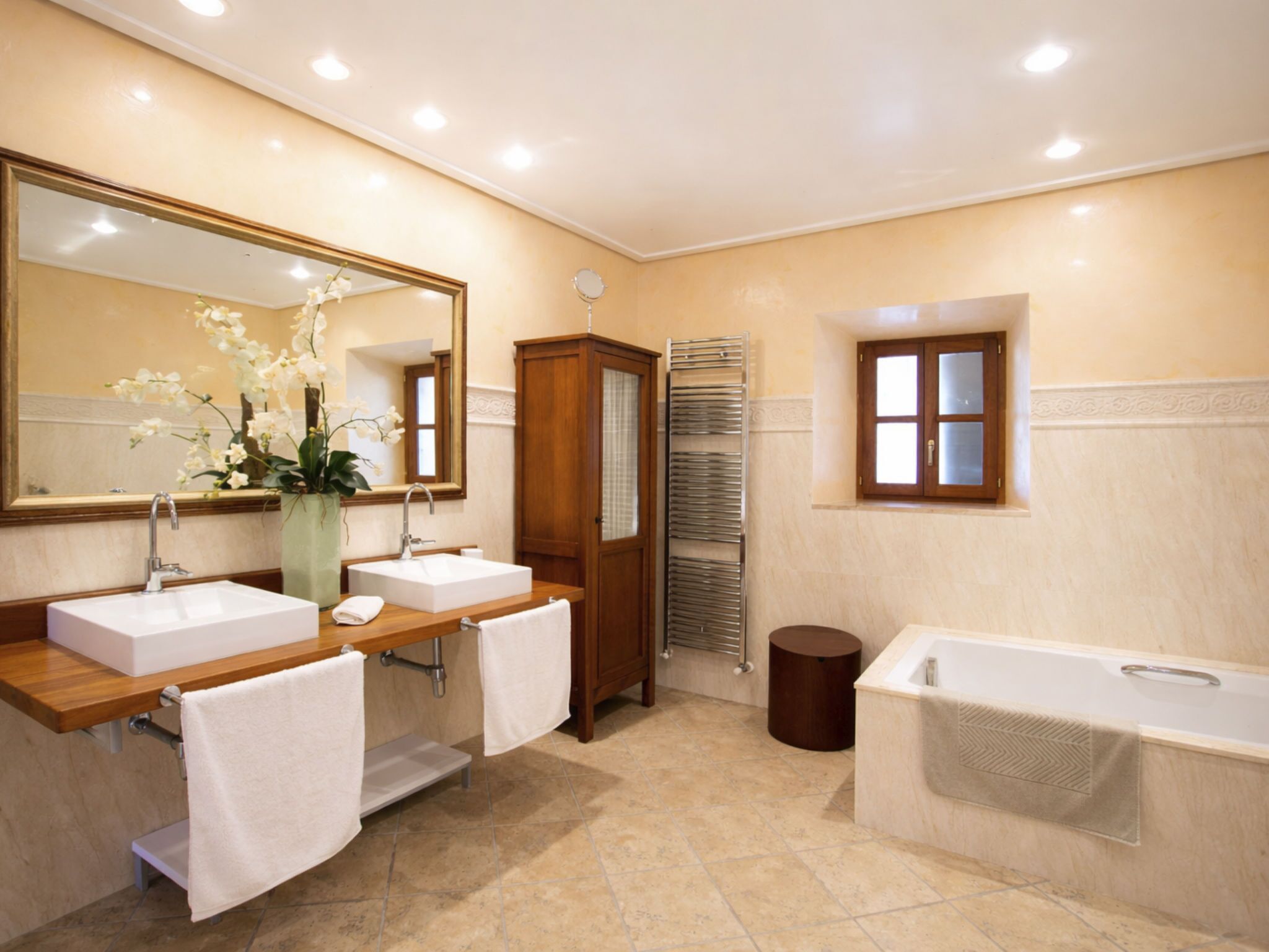 A bathroom with two sinks, a large mirror, a wooden cabinet, a towel rack, a bathtub, and a window.