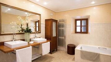 A bathroom with two sinks, a large mirror, a wooden cabinet, a towel rack, a bathtub, and a window.