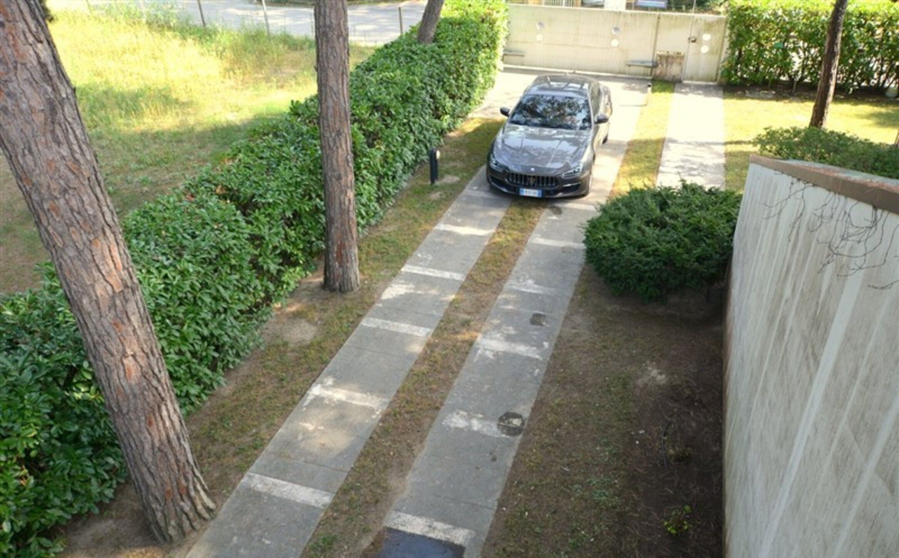 Une voiture était garée sur une allée étroite, bordée d’un trottoir d’un côté et d’une clôture de l’autre.