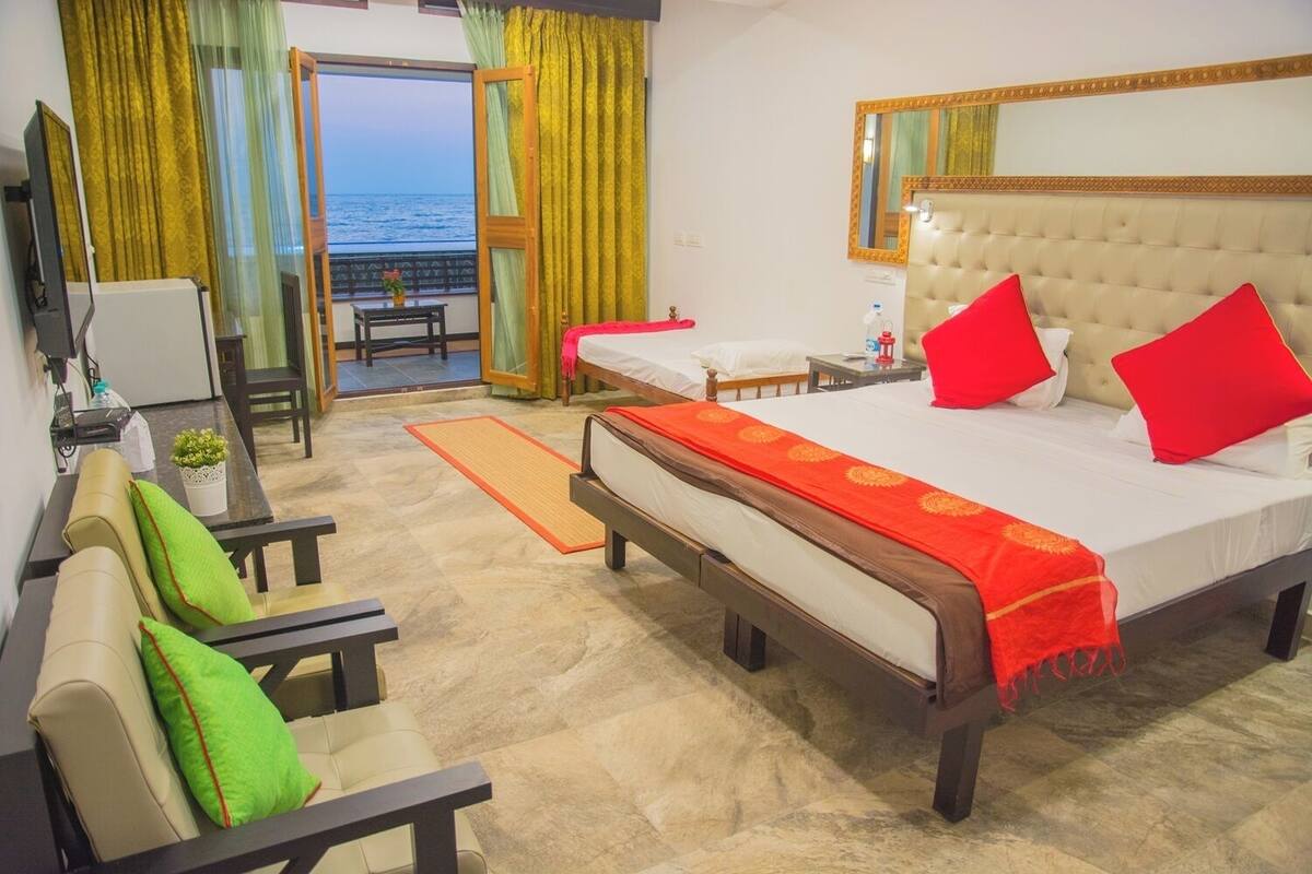A hotel room with a bed, a sofa, a desk, a chair, and a view of the sea through a window.