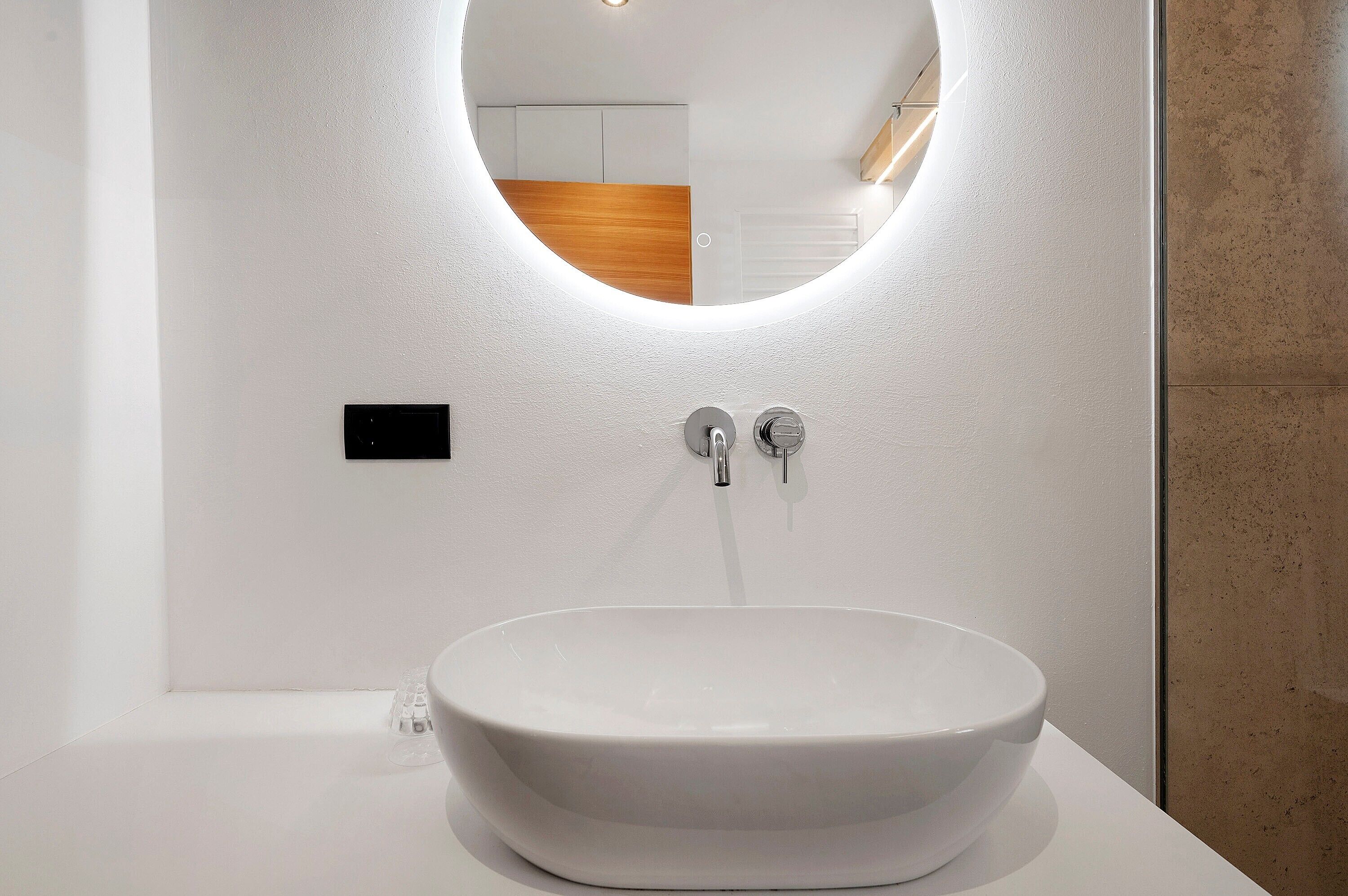 Ein modernes Badezimmer mit einem weißen Waschbecken, einem runden Spiegel und einer Holzvertäfelung im Hintergrund.