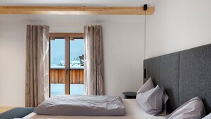 Ein Schlafzimmer mit Bett, Kissen, Kopfteil, einem Fenster mit Vorhängen und Blick auf eine verschneite Landschaft.