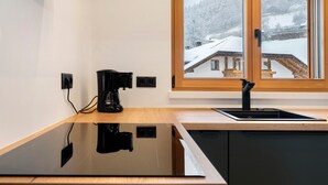 Eine moderne Küche mit einer schwarzen Kaffeemaschine, einem Spülbecken und einem Fenster mit Blick auf eine verschneite Landschaft.