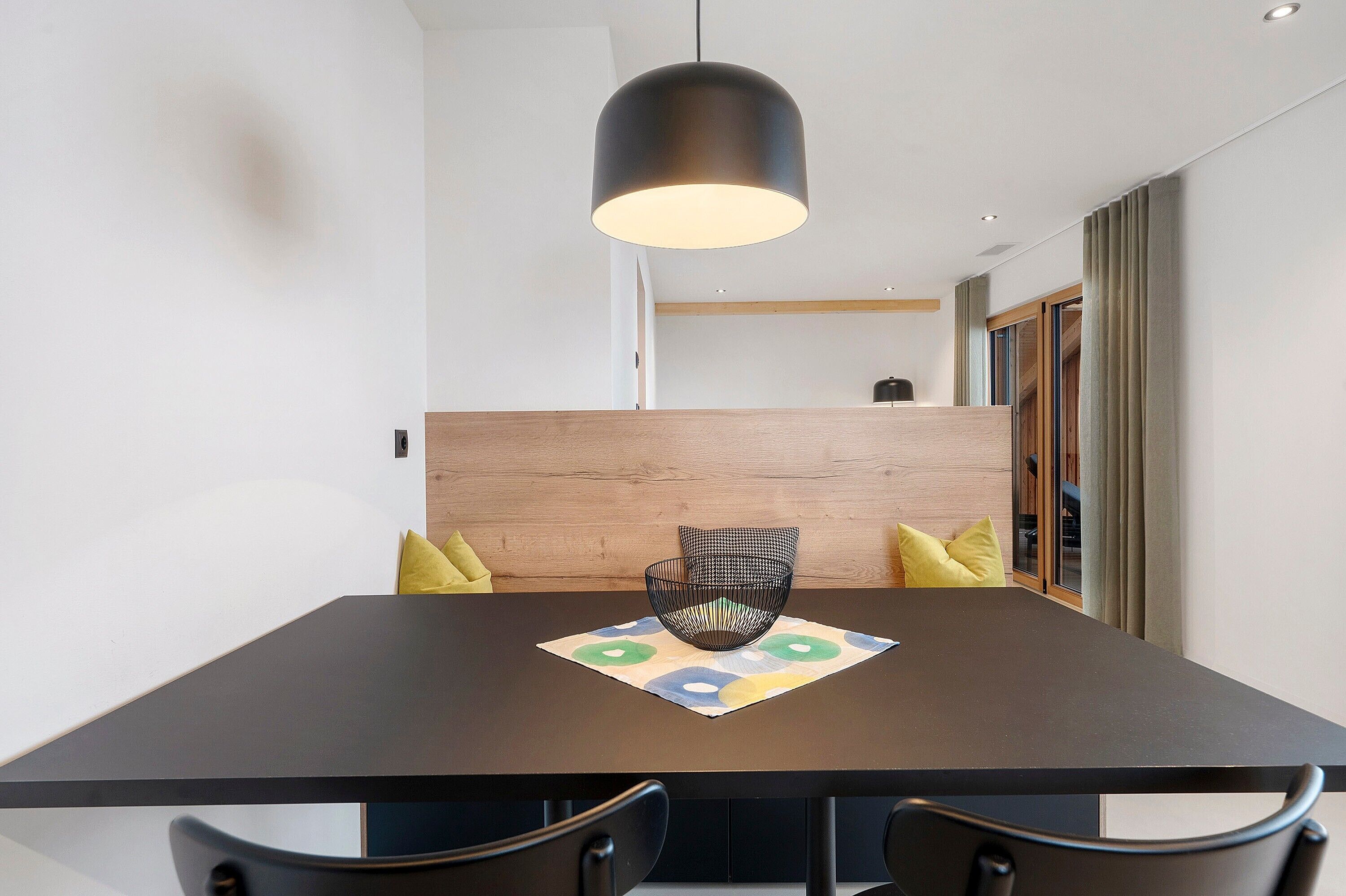 A modern dining area with a dark wooden table, black chairs, a black pendant light, and a colorful placemat.