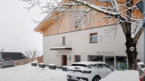 Ein Gebäude mit Holzfassade, ein Auto davor und Schnee auf dem Boden.