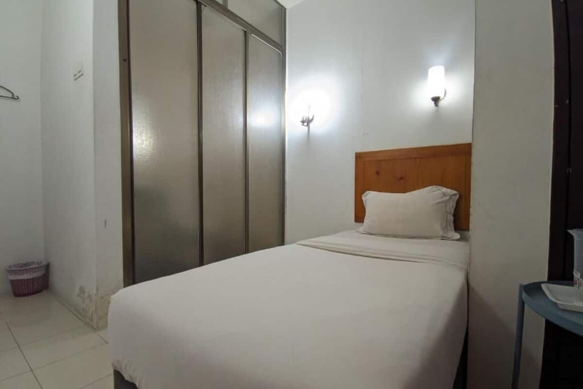 A single-bed room with a wooden headboard, a small bedside table, and a wall-mounted light fixture.
