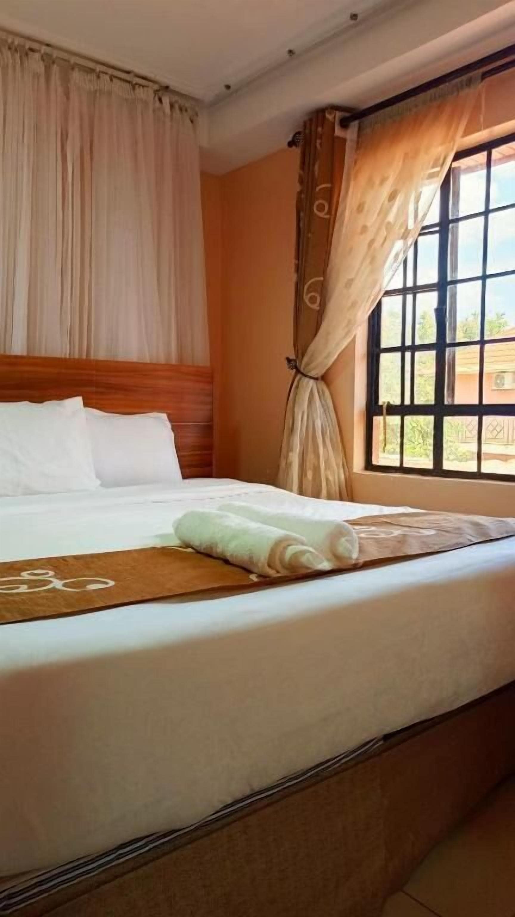 A neatly made bed with white linens, a wooden headboard, and a window with curtains.