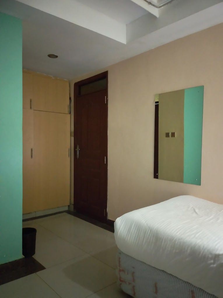 Un dormitorio con cama, armario, puerta y espejo en la pared.