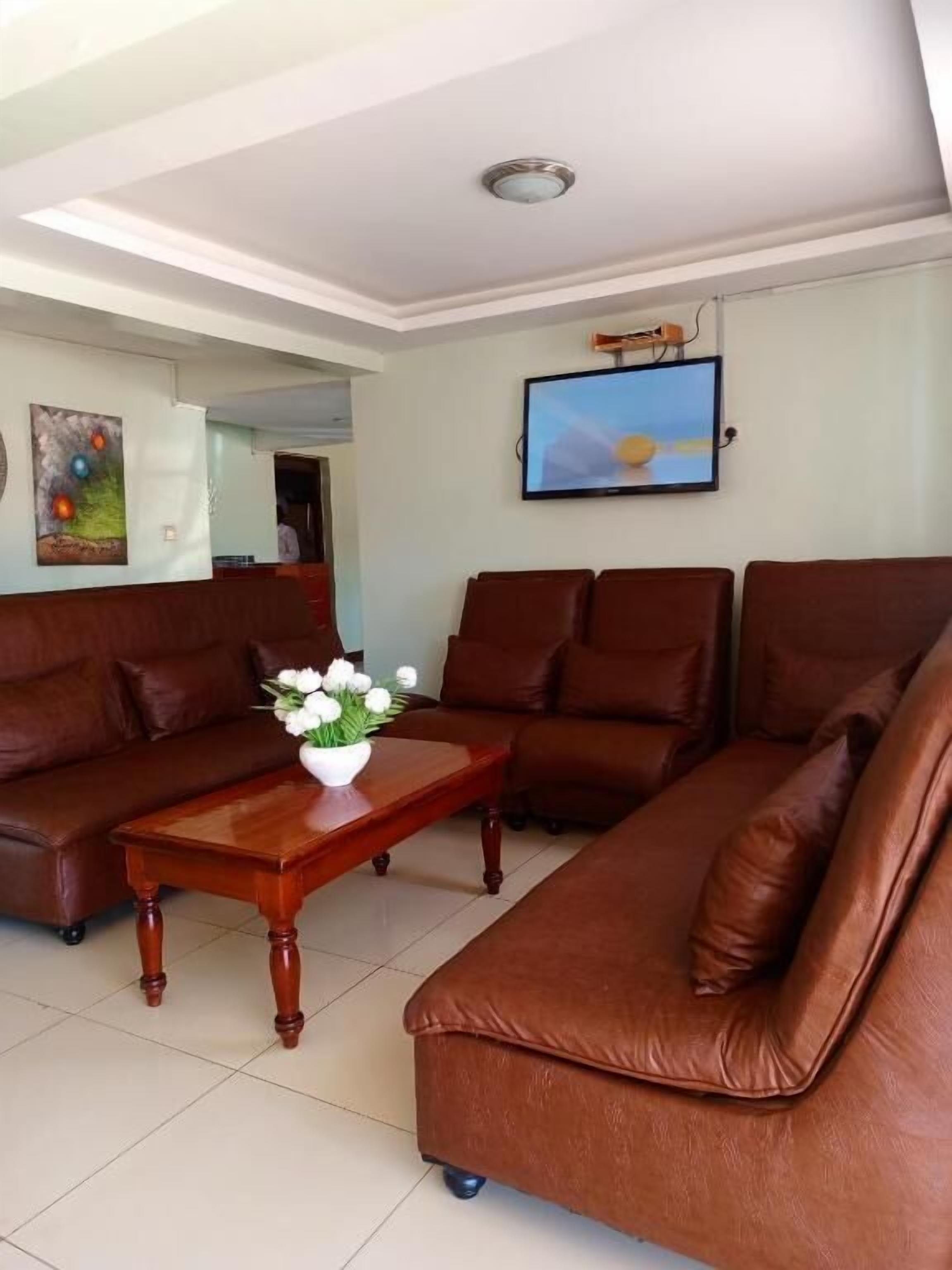 Un salón con un sofá de cuero marrón, una mesa de centro de madera con un florero y un televisor de pantalla plana montado en la pared.