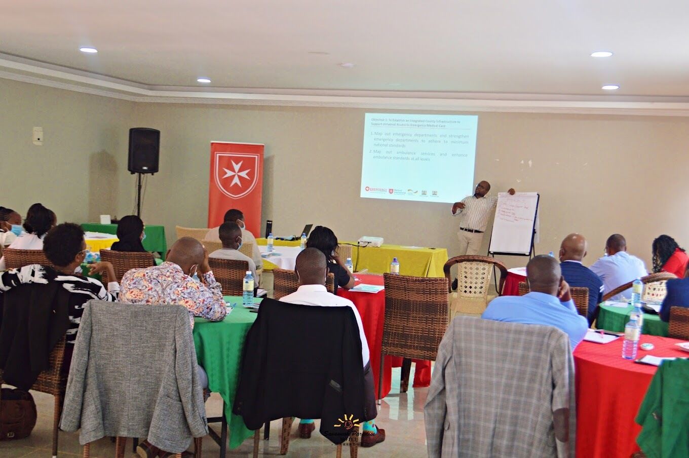 A conference room with attendees seated at tables, a presentation screen, and a speaker at the front.