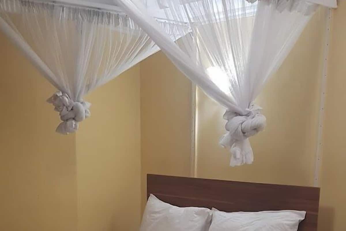 Un lit bien fait, avec des draps blancs, une tête de lit en bois et une moustiquaire au-dessus.