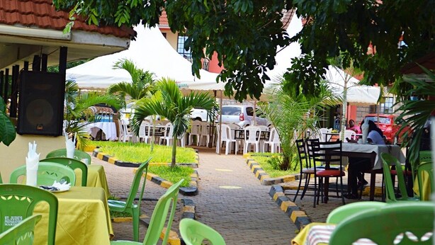 An outdoor seating area with green plastic chairs and tables, a paved walkway, and a white tent in the background. - Savannah Paradise Hotel Makindu (Makindu)
