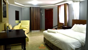 A hotel room with a bed, a desk, a chair, a wardrobe, and a door. - Savannah Paradise Hotel Makindu (Makindu)