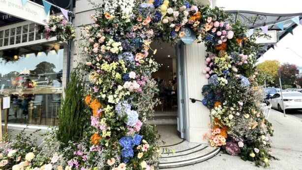 Ein Gebäudeeingang mit einem floralen Bogen und einem Schild mit der Aufschrift "THE PRESS SHOP".