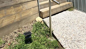 Ein modernes Gebäude mit einer Treppe, die zu einem überdachten Bereich führt, umgeben von Kies und Topfpflanzen.