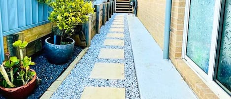 Uma trilha estreita com pedras para caminhar, ladeada por uma cerca azul e um edifício de tijolos.
