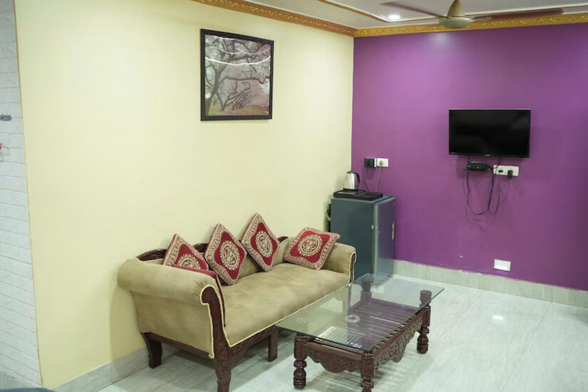 A living room with a sofa, a glass coffee table, a television mounted on a purple wall, and a ceiling fan.