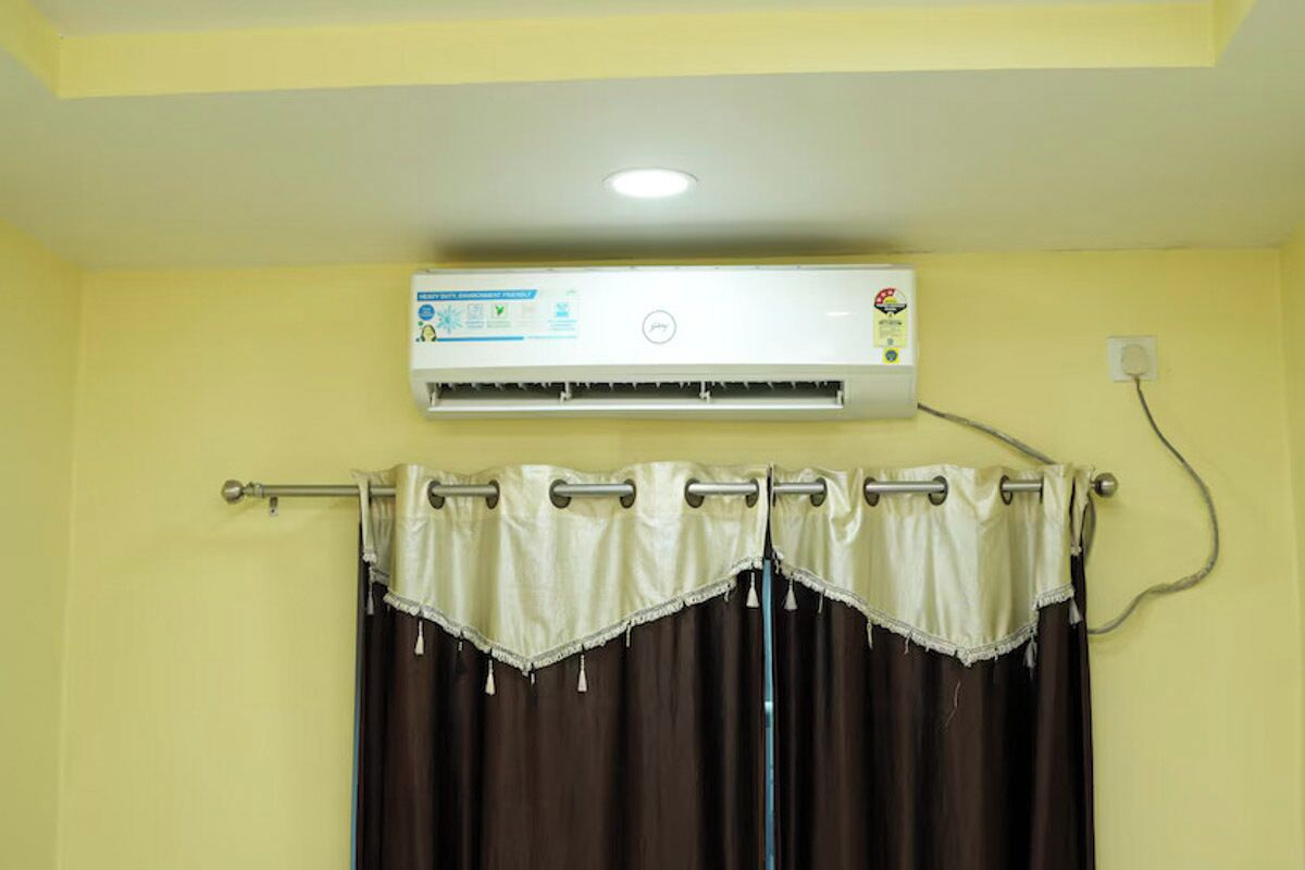 A room with a ceiling-mounted air conditioner, a curtain rod with a curtain, and a wall socket.
