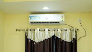 A room with a ceiling-mounted air conditioner, a curtain rod with a curtain, and a wall socket.