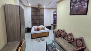 A compact hotel room with a bed, a sofa, a small table, and a mirror. - Hotel DL (Tezpur)