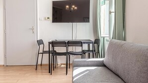 A room with a TV mounted on the wall, a dining table with chairs, and a sofa. - Cozy 2BR Apartment Near Prater Danube (Vienna)