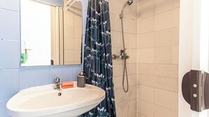 A bathroom with a white sink, a mirror, a shower with a floral curtain, and beige tiled walls. - Cozy 2BR Apartment Near Prater Danube (Vienna)