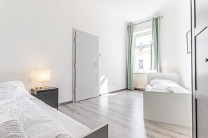 Un dormitorio con dos camas, una mesita de noche con lámpara, un armario y una ventana con cortinas.