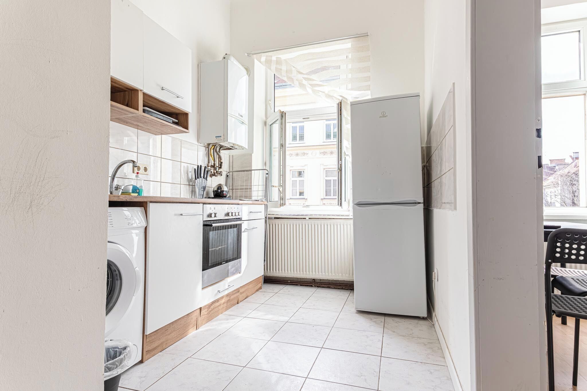 Cocina compacta con electrodomésticos blancos, horno integrado y ventana con vistas a la ciudad.