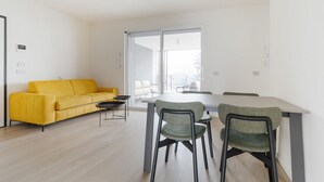 A modern living room with a yellow sofa, a dining table with chairs, and a sliding glass door leading to a balcony. - GuestHost - Spacious and modern 75 square meters apartment, perfect for six people, located on the second floor of a building with an elevator (NOT accessible to guests with disabilities).The property is located in a quiet area, allowing our guests to ex (Milan)