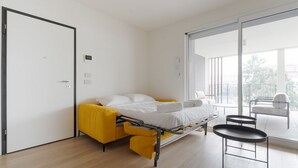 A modern bedroom with a bed, a yellow sofa, a small table, and a sliding glass door leading to a balcony. - GuestHost - Spacious and modern 75 square meters apartment, perfect for six people, located on the second floor of a building with an elevator (NOT accessible to guests with disabilities).The property is located in a quiet area, allowing our guests to ex (Milan)