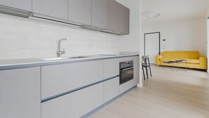 A modern kitchen with grey cabinets, a built-in oven, and a yellow sofa in the living area. - GuestHost - Spacious and modern 75 square meters apartment, perfect for six people, located on the second floor of a building with an elevator (NOT accessible to guests with disabilities).The property is located in a quiet area, allowing our guests to ex (Milan)