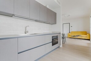 Eine moderne Küche mit grauen Schränken, einem eingebauten Backofen und einem gelben Sofa im Wohnbereich.