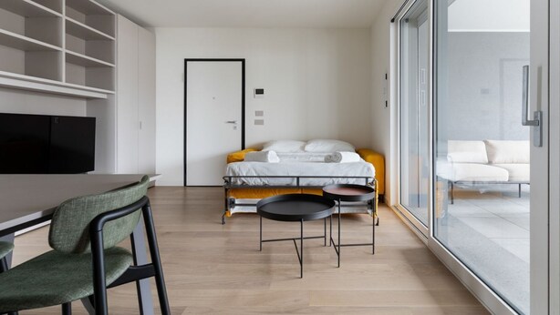 A modern hotel room with a bed, a dining table, chairs, a TV, and a large window. - GuestHost - Spacious and modern 75 square meters apartment, perfect for six people, located on the second floor of a building with an elevator (NOT accessible to guests with disabilities).The property is located in a quiet area, allowing our guests to ex (Milan)