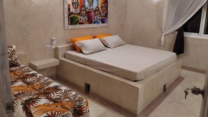 Un dormitorio con cama, mesitas de noche, un sofá, un cuadro y una ventana con cortinas.