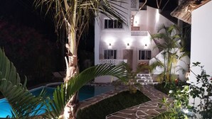 Un espace extérieur bien éclairé, doté d’une piscine, d’un chemin en pierre et d’un immeuble à plusieurs étages dont les fenêtres sont illuminées.