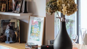 Una habitación moderna con un escritorio de madera, un florero con flores secas, un cuadro enmarcado y un estante con diversos objetos.