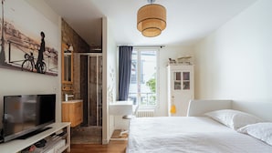 Un dormitorio moderno con una cama grande, televisión, armario y ventana con cortinas.