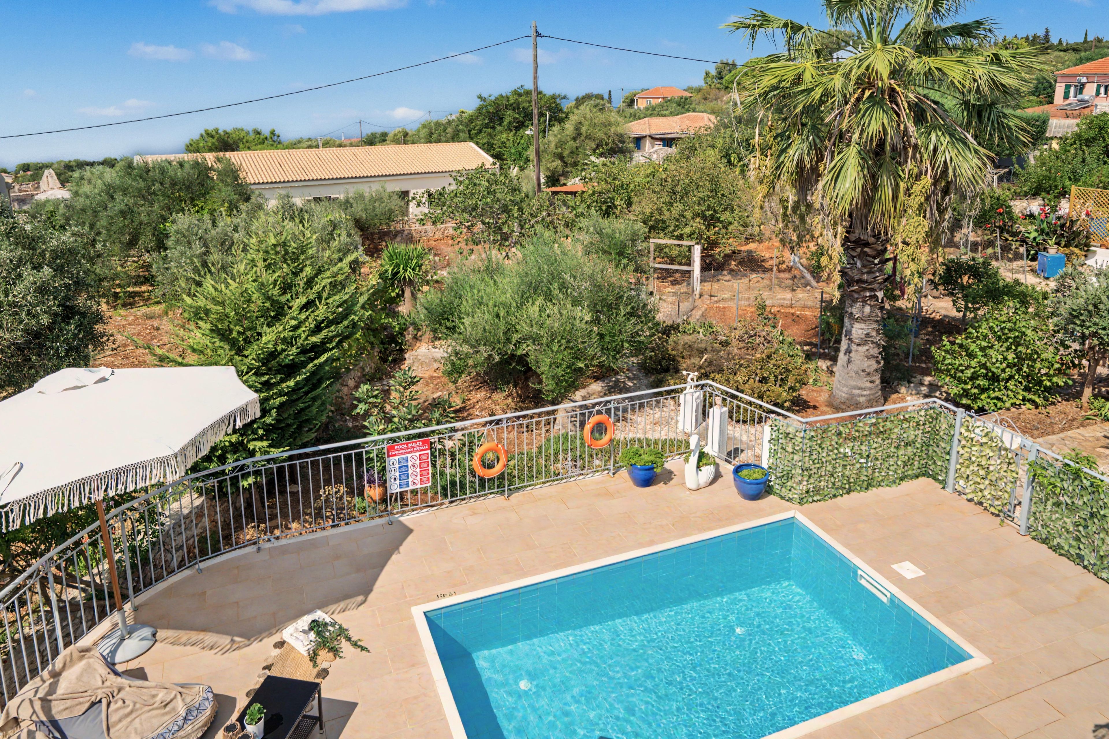 Piscina retangular com borda azulejada, rodeada por uma cerca de metal e um guarda-sol branco.