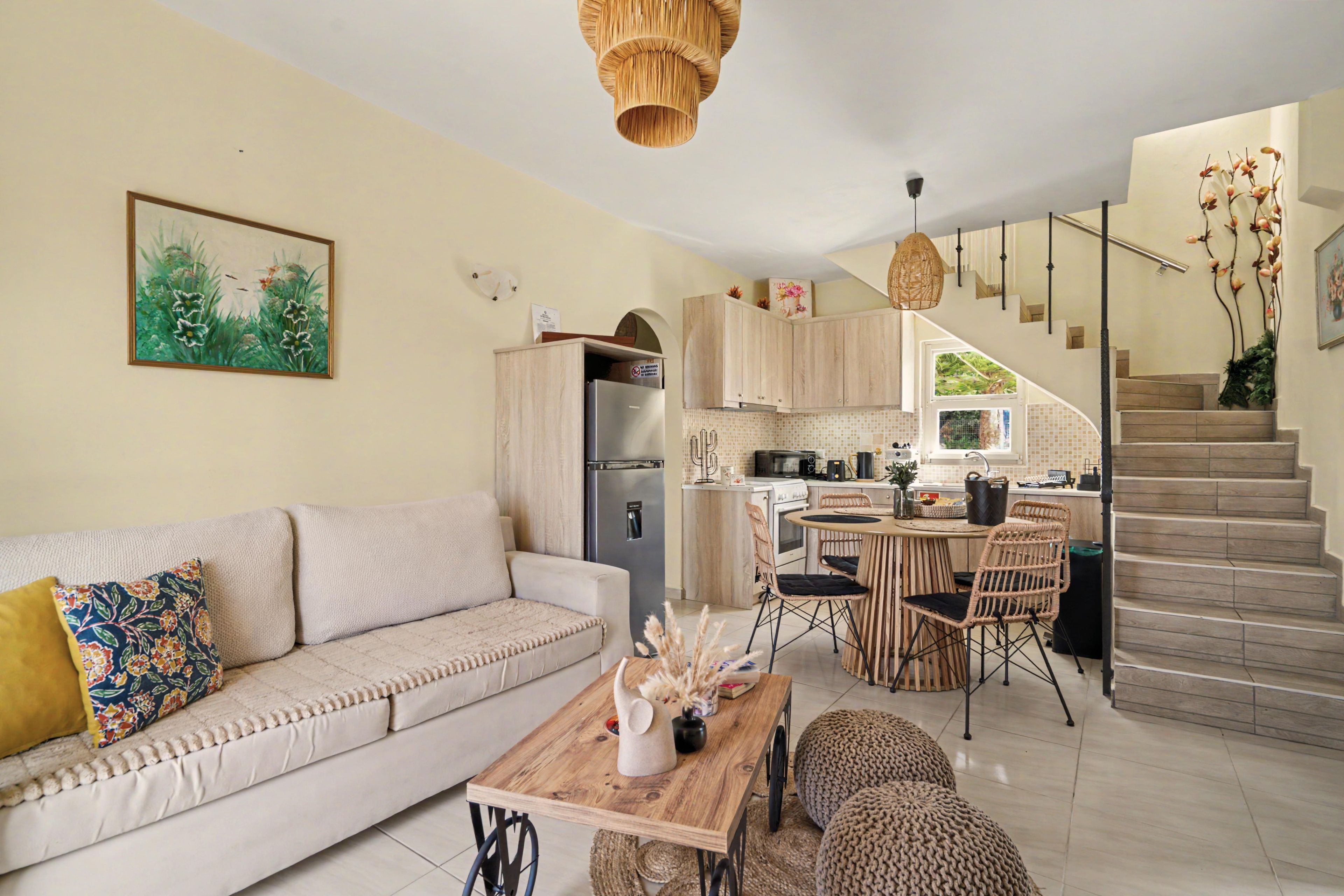 Un soggiorno moderno con divano, tavolino e zona pranzo con sedie. Si intravede una cucina con elettrodomestici e una scala che conduce a un piano superiore.