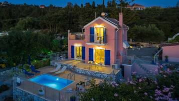 Ein zweistöckiges Haus mit Swimmingpool, Sitzgelegenheiten im Freien und einem Balkon.