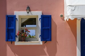 Un bâtiment doté d’une fenêtre ornée de volets bleus, d’un pot de fleurs contenant des fleurs rouges et d’un luminaire fixé au mur.