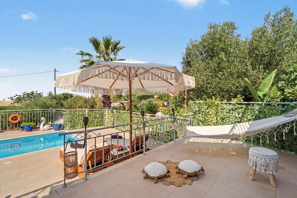 A poolside area with a hammock, two cushions, and a large umbrella.