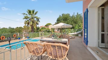 A balcony with a pool, wicker furniture, and a view of the surrounding area.