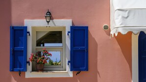 Una ventana con contraventanas azules, una planta en maceta y un toldo blanco.