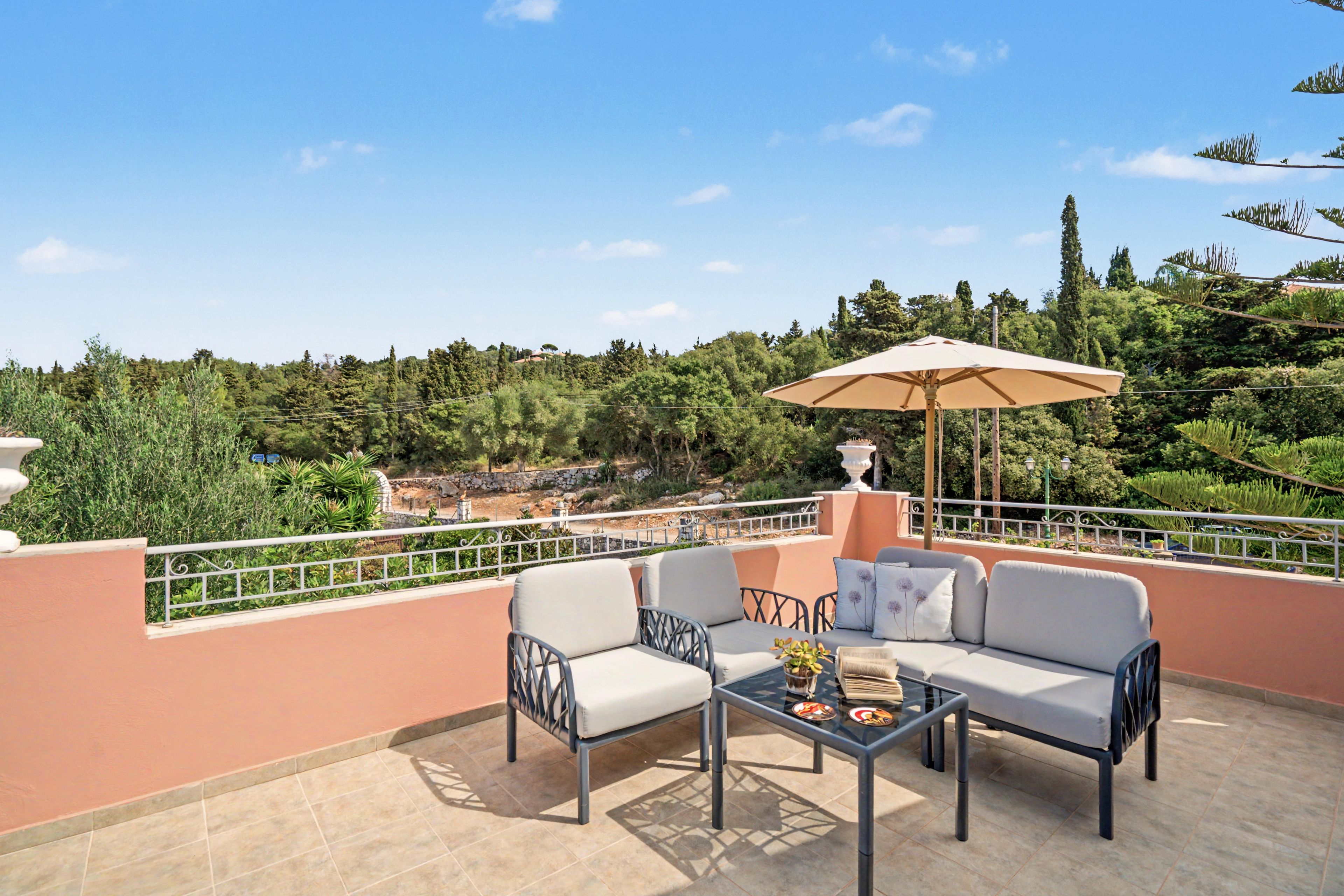 Una terrazza con divano, sedie e tavolo, affacciata su un paesaggio pittoresco con alberi e una collina.