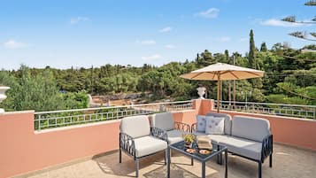 Una terrazza con divano, sedie e tavolo, affacciata su un paesaggio pittoresco con alberi e una collina.