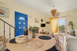 A room with a blue door, a round table with woven placemats, wicker chairs, a sofa, and a view through a yellow curtain to an outdoor area with plants.