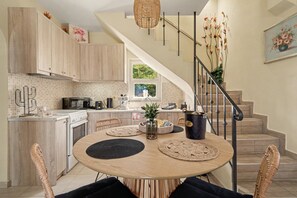Une cuisine moderne avec des meubles en bois, une table à manger agrémentée de sets de table en fibres tressées et un escalier doté d’une rampe.
