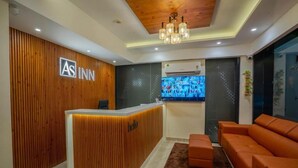 A hotel reception area with a wooden reception desk, a large TV screen, and a seating area with orange sofas. - AS Inn (Kanayannur)