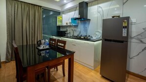 A compact kitchen with a dining area, featuring a modern design with a glass table, wooden chairs, a built-in oven, and a refrigerator. - AS Inn (Kanayannur)